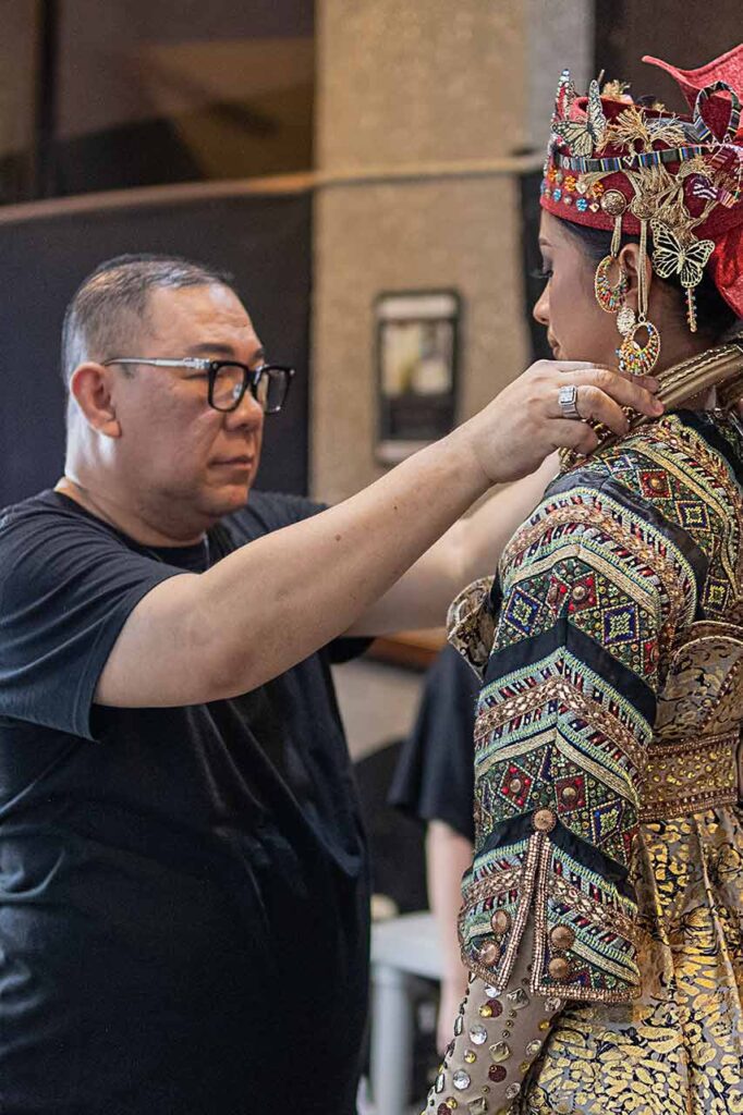 Amir Sali adjusts an ornate costume worn by a model before a cultural fashion presentation