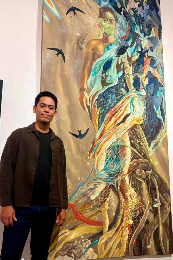Hersley Casero standing beside one of his large-scale artworks in a gallery