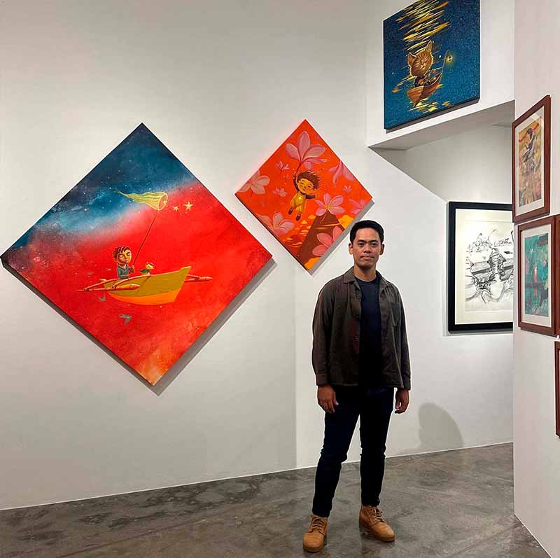 Hersley Casero standing in a gallery surrounded by several of his colorful artworks