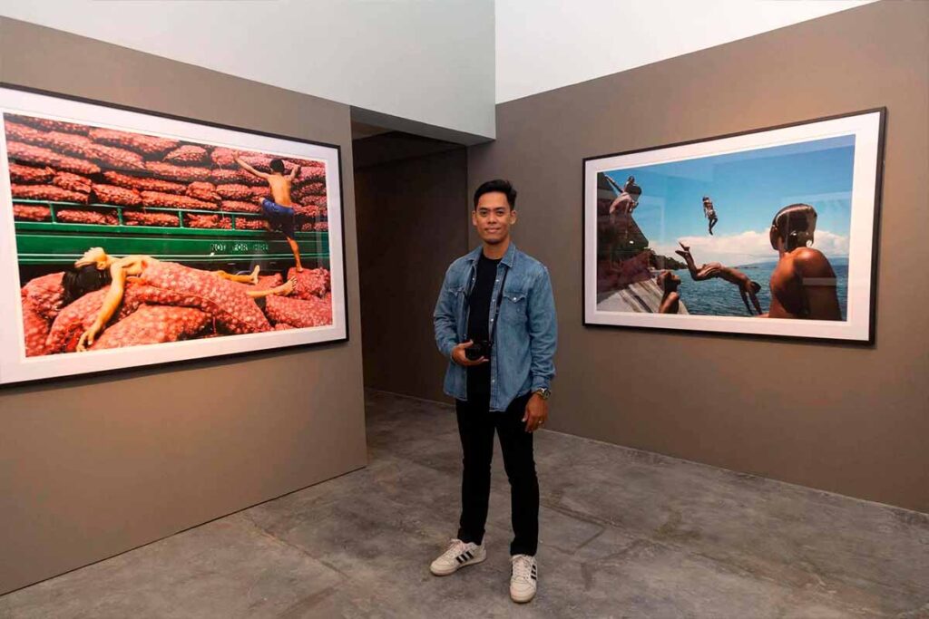 Filipino photographer Hersley-Ven Casero standing between two large framed photographs at his exhibition