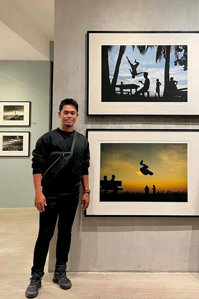 Hersley-Ven Casero standing beside two framed photographs featuring silhouettes of people against the sky