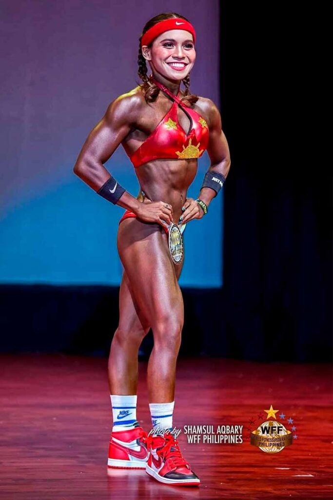 Julianna Nicole Lopez posing on stage in a red sports model outfit during a WFF Philippines competition