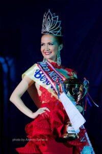 Monica Infante Bartsch smiling in a red gown with her crown, winner's sash, and trophy at Miss Negros Oriental Tourism 2013