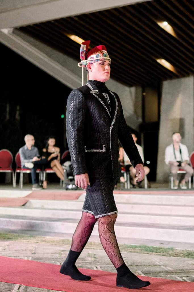 Male model in a black tailored runway look with decorative headpiece from Amir Sali’s collection
