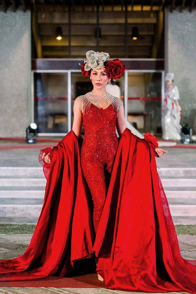 Model wearing a red embellished evening gown with a dramatic train from Amir Sali’s collection